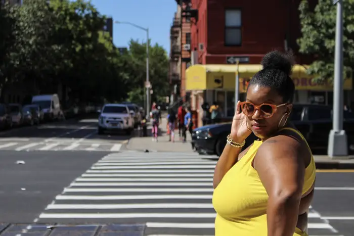 a woman in a yellow shirt poses on a Harlem street